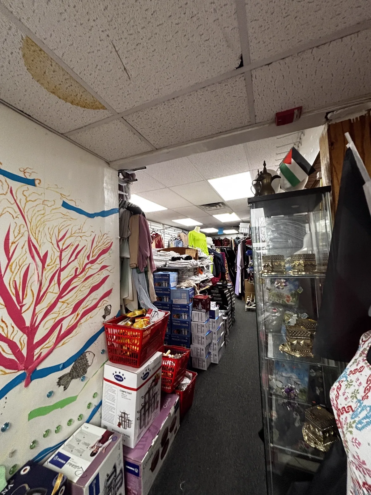 Entrance to the bazaar inside Makkah Market — coral mural, Palestinian flag and shelves of brass and glass items