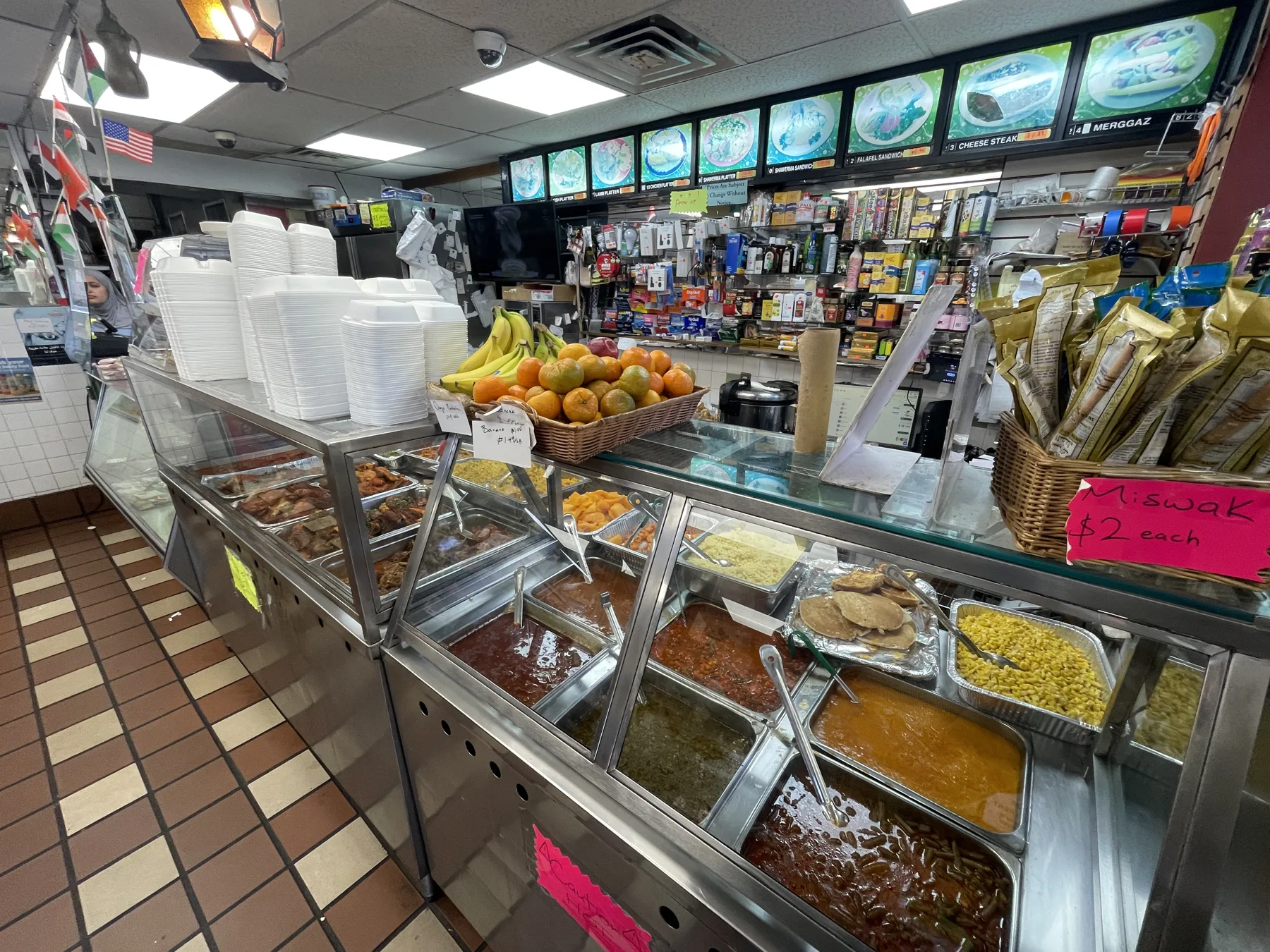 The hot-food counter at Makkah Market — steam trays of rice, stews, vegetables and grilled meats with the numbered menu board behind